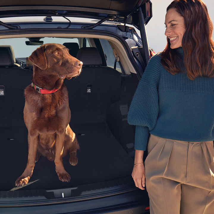 Widok z tyłu na hybrydową Hondę CR-V z psem i modelem siedzącym w bagażniku.