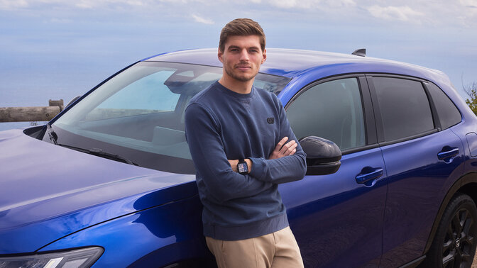 Max Verstappen opierający się o zaparkowanego niebieskiego hybrydowego SUVa Honda ZR-V.