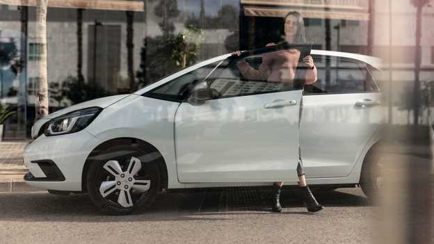 Widok z boku na zaparkowaną Hondę Jazz i kobietę otwierającą drzwi