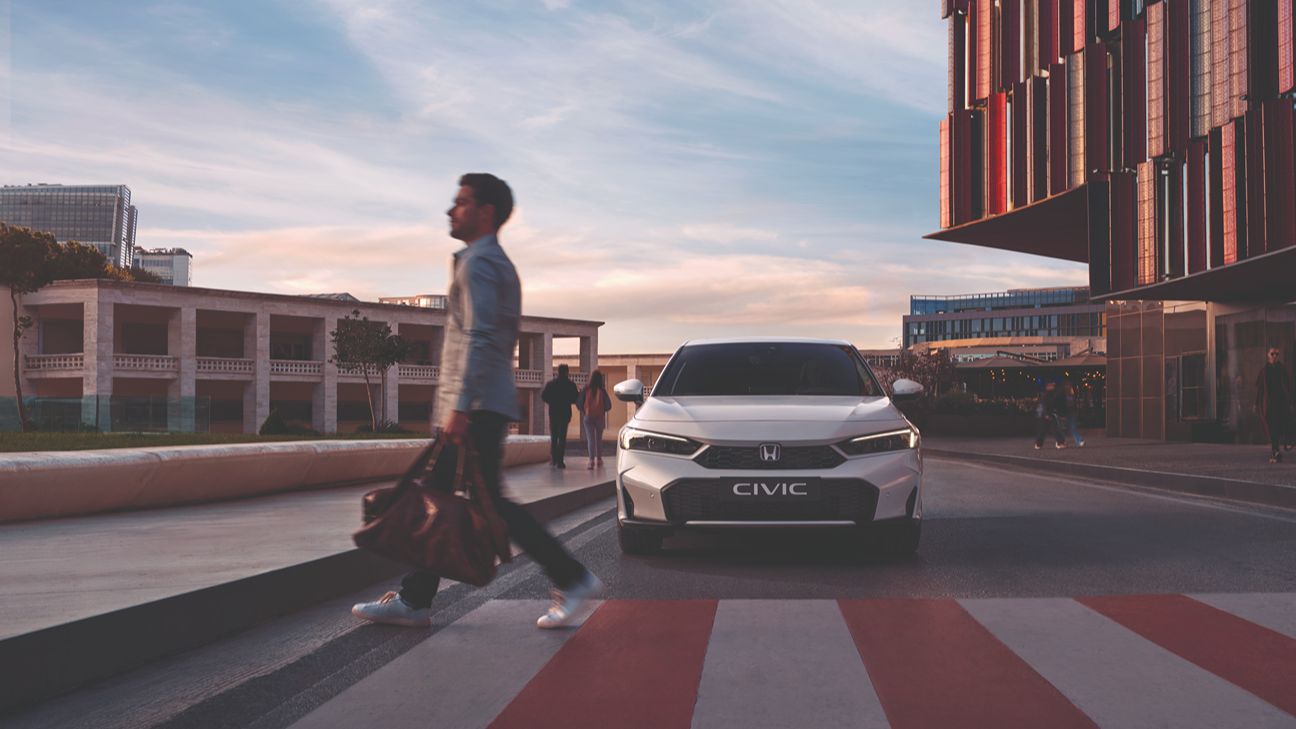 Mężczyzna przechodzący przez ulicę z białą Hondą Civic z tyłu