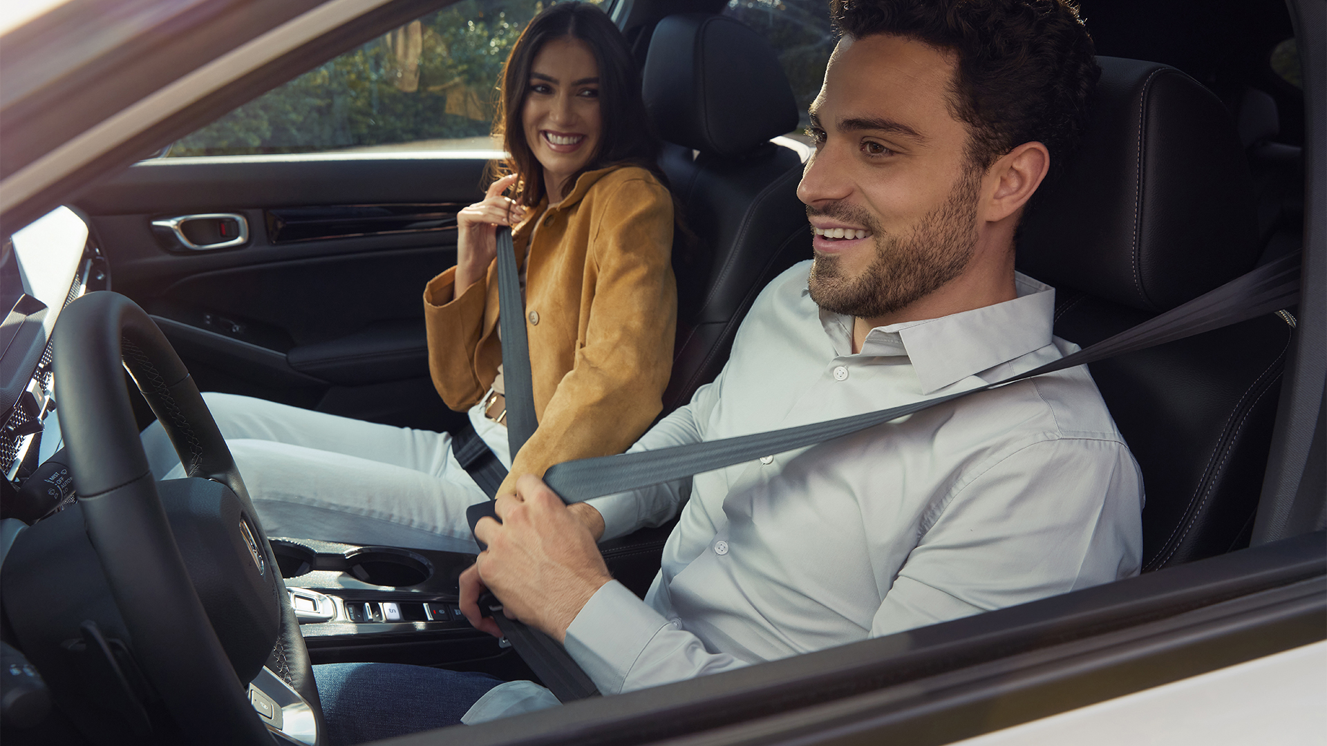 Dwie osoby zapinające pasy bezpieczeństwa wewnątrz Hondy Civic Hybrid.