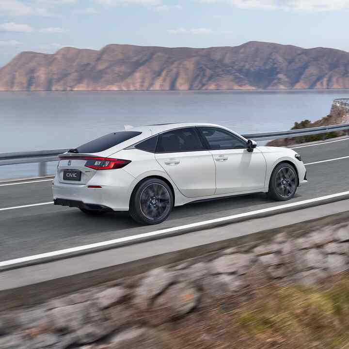 Side view of the Honda Civic e:HEV driving down a coastal road.