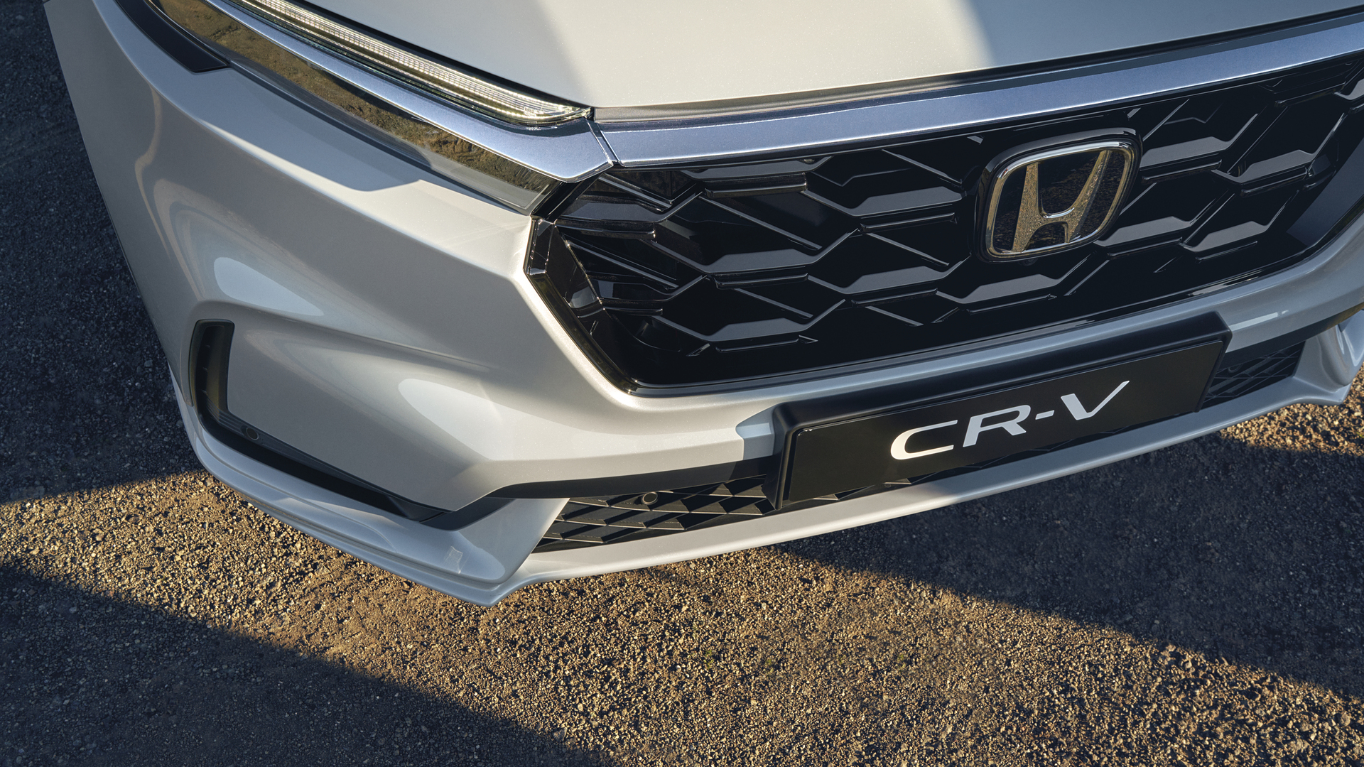 Zbliżenie na przednią osłonę chłodnicy Honda CR-V, charakteryzującą się czarnym wzorem w plastry miodu, z logo Honda pośrodku oraz nazwą modelu CR-V widoczną poniżej.