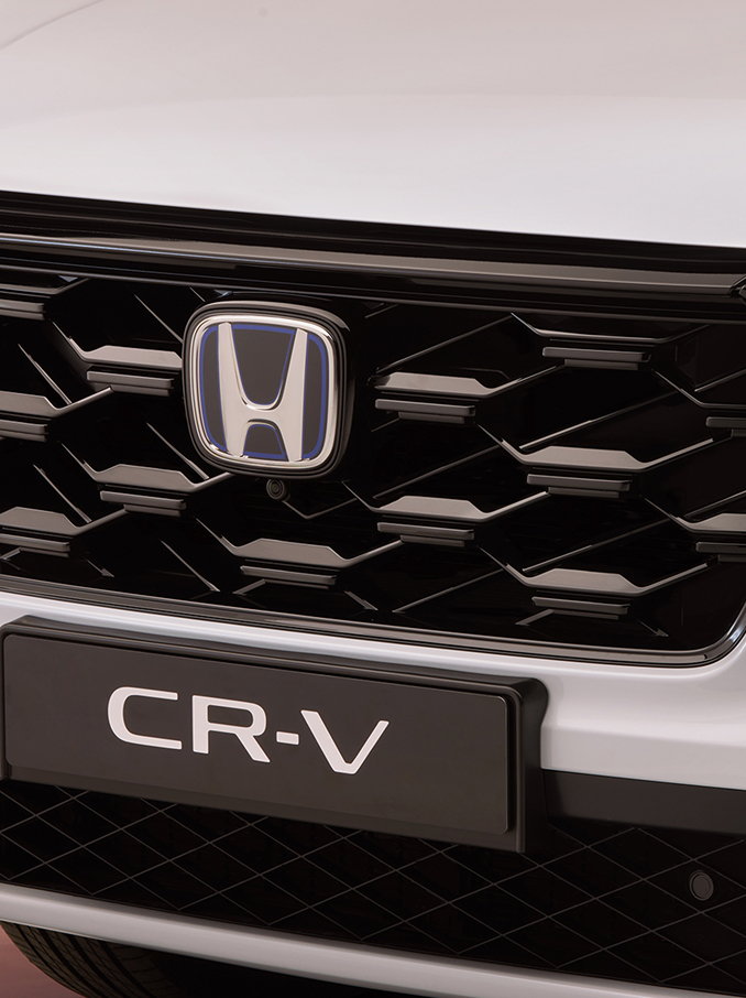 Zbliżenie na przednią osłonę chłodnicy Honda CR-V, charakteryzującą się czarnym wzorem w plastry miodu, z logo Honda pośrodku oraz nazwą modelu CR-V widoczną poniżej.