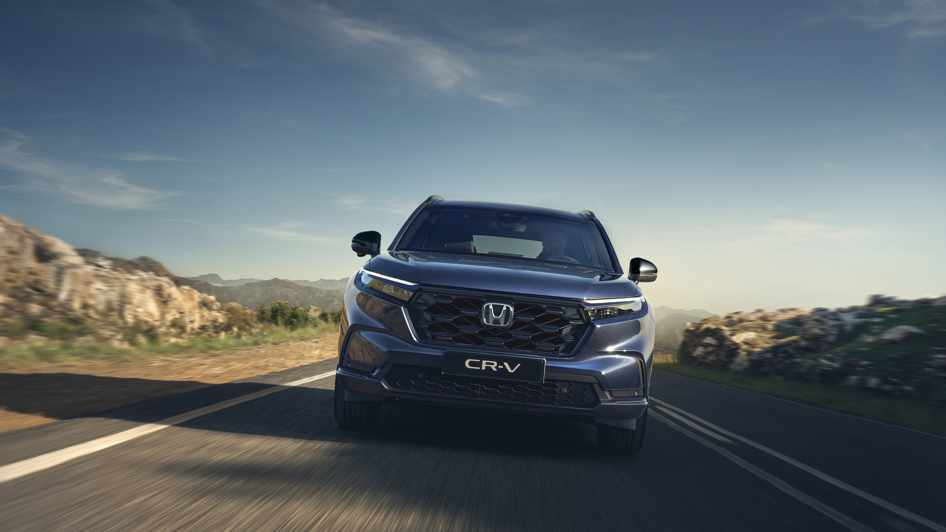 Honda CR-V jedzie krętą górską drogą pod czystym, błękitnym niebem.