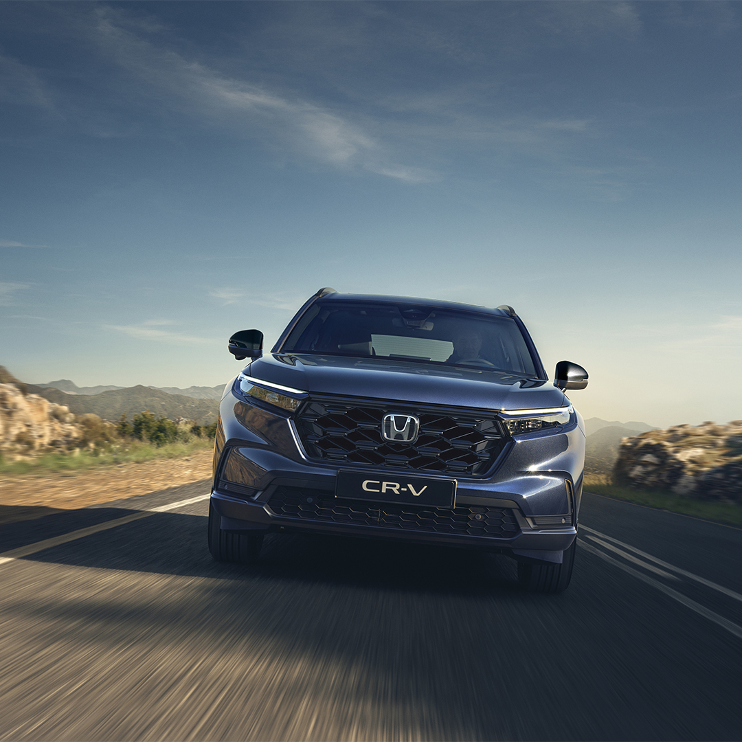 Honda CR-V jedzie krętą górską drogą pod czystym, błękitnym niebem.