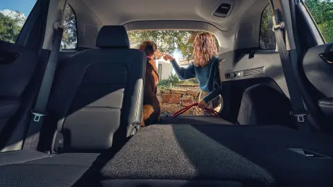 Hybrydowy SUV CR-V - rozłożone tylne siedzenie z kobietą i psem w otwartym bagażniku. 