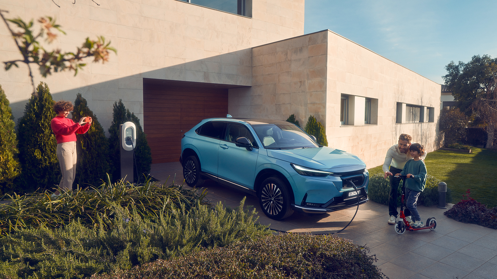 Rodzina bawiąca się na podjeździe obok Hondy e:Ny1 podłączonej do ładowania.