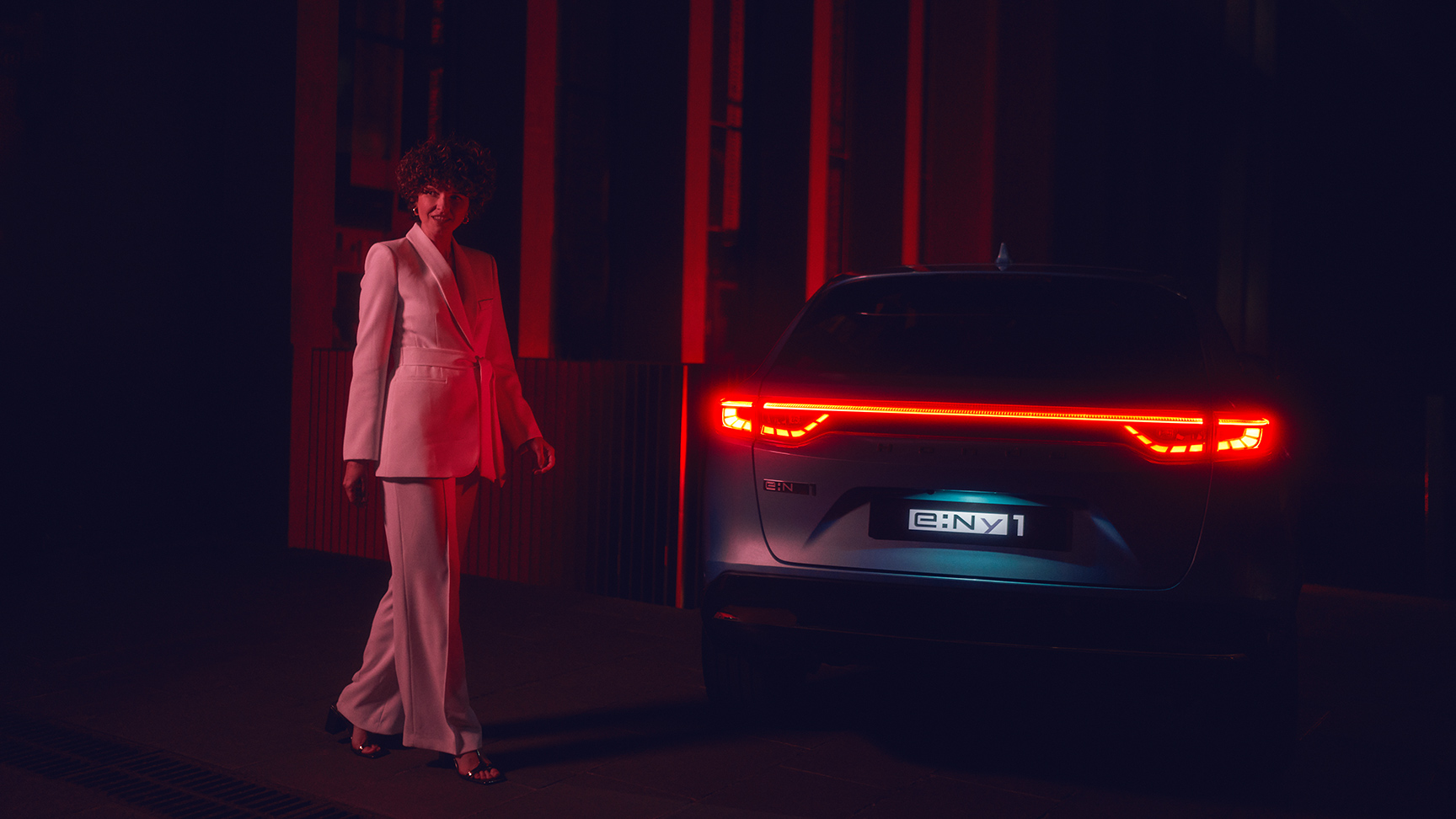 Model stojący obok oświetlonego tyłu Hondy e:Ny1 w nocy.