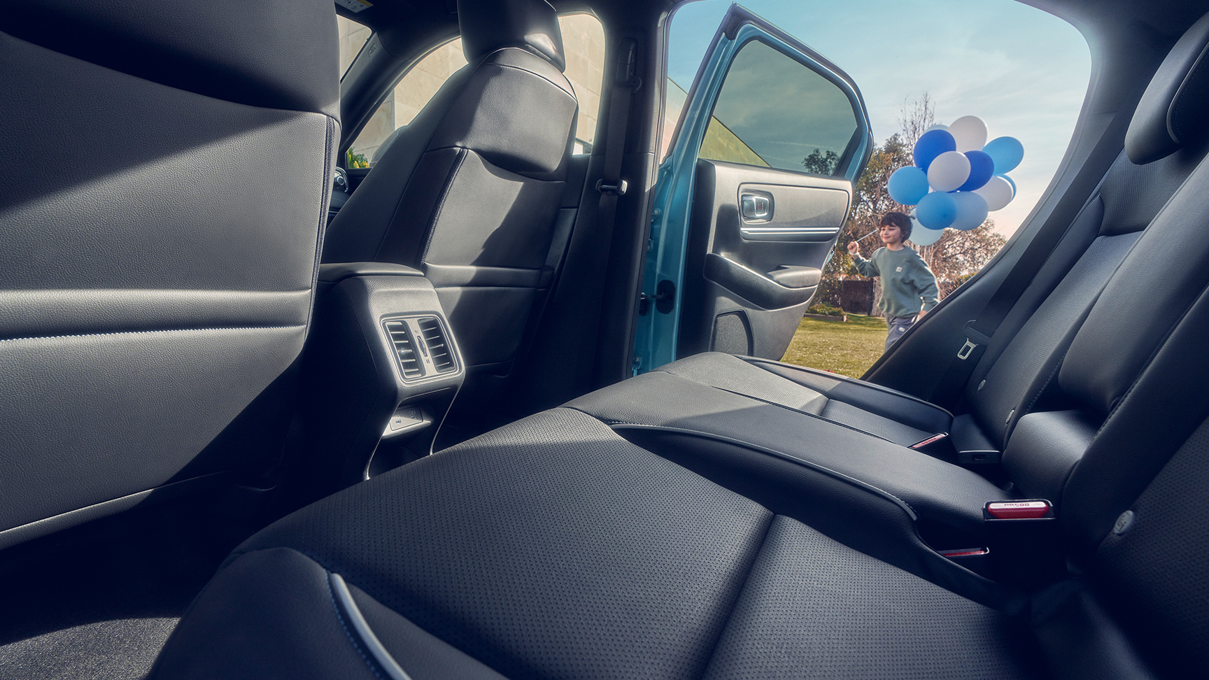 Zbliżenie na tylne siedzenie Hondy e:Ny1 z dzieckiem przechodzącym obok otwartych drzwi i niosącym balony.
