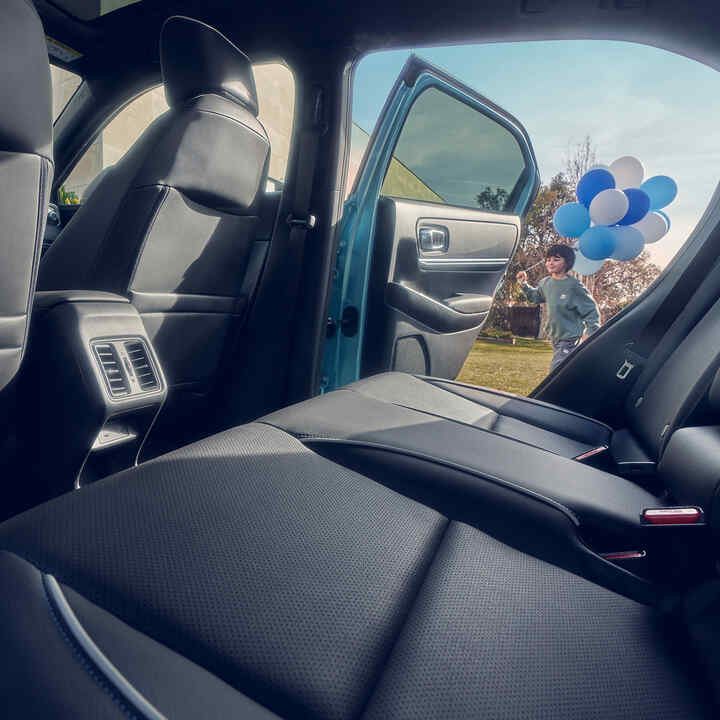 Zbliżenie na tylne siedzenie Hondy e:Ny1 z dzieckiem przechodzącym obok otwartych drzwi i niosącym balony.