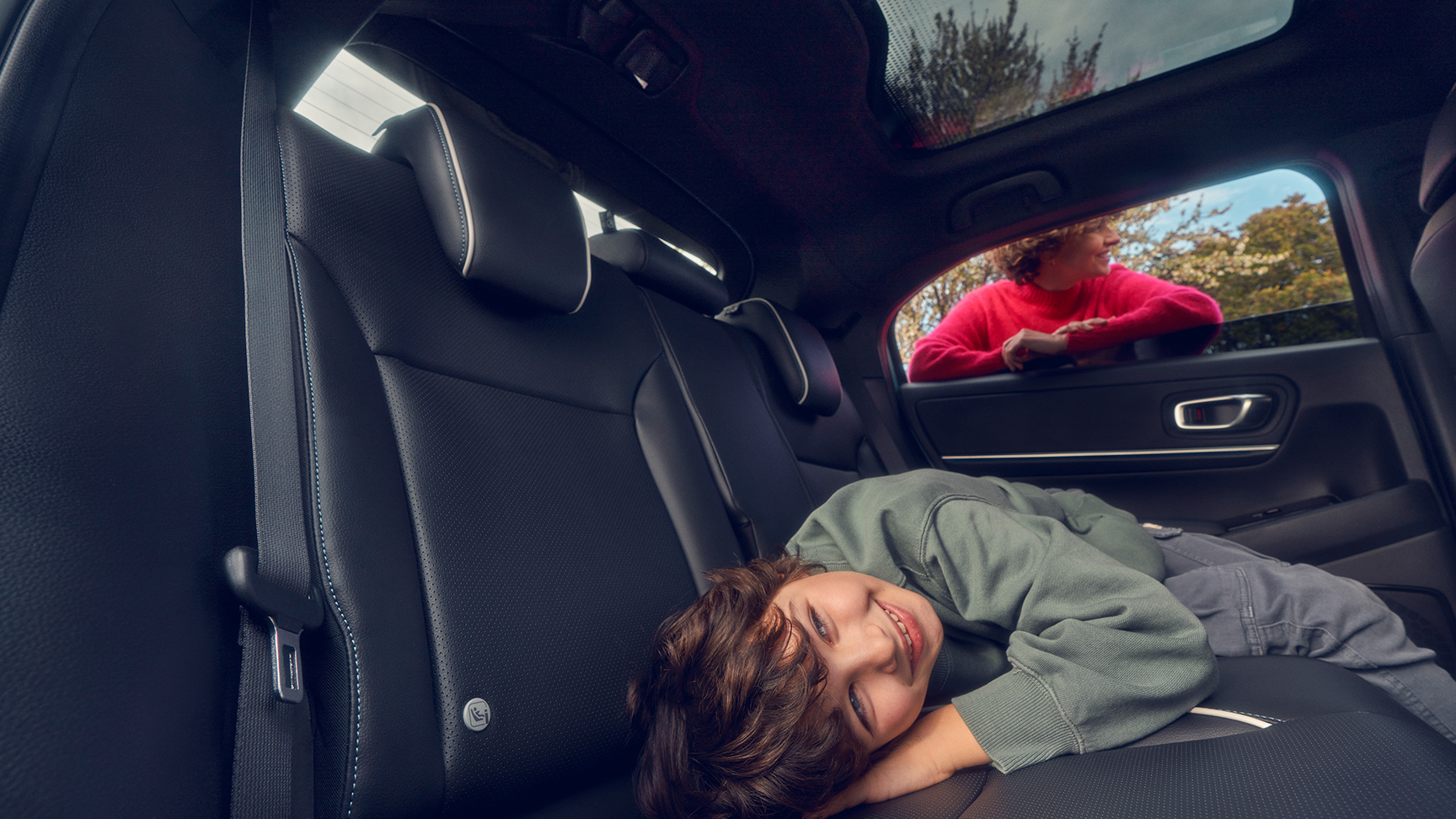 Dziecko leżące na tylnym siedzeniu z matką stojącą przy oknie Hondy e:Ny1.