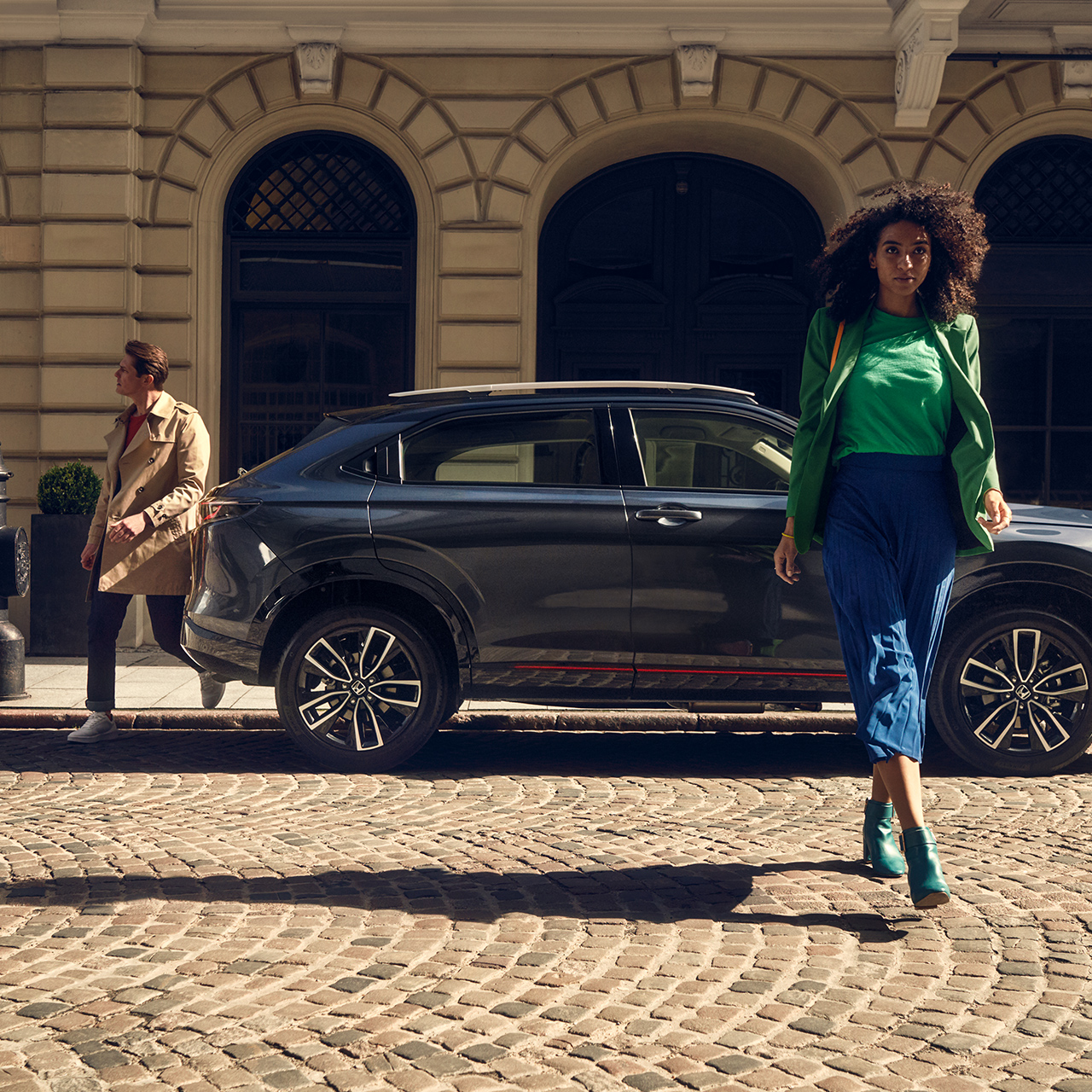Model idący przed hybrydową Hondą HR-V zaparkowaną w mieście.