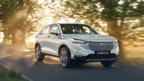 Hybrydowa Honda HR-V jadąca drogą w otoczeniu wiejskiego krajobrazu.