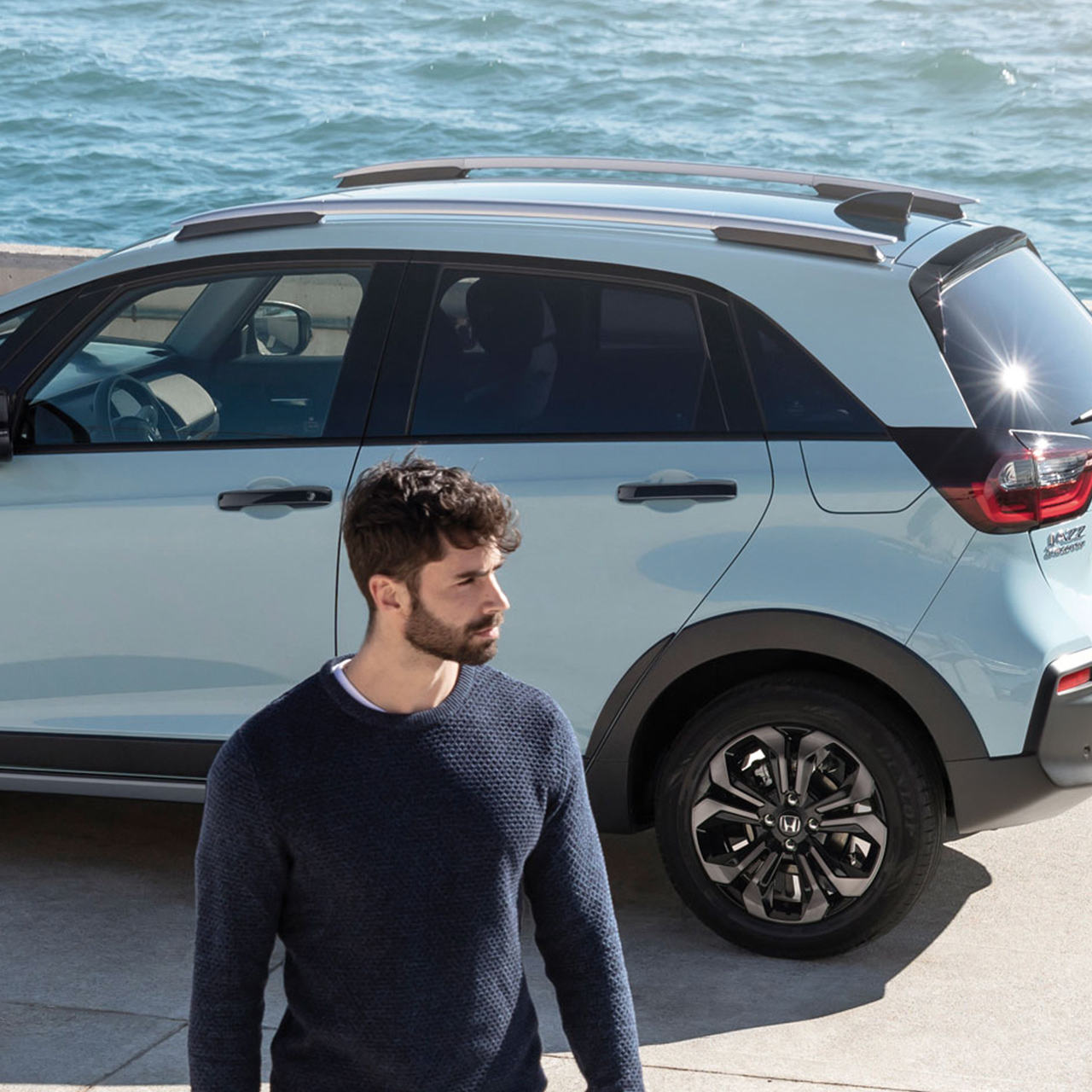 Model spacerujący przed Hondą Jazz Crosstar zaparkowaną nad morzem.