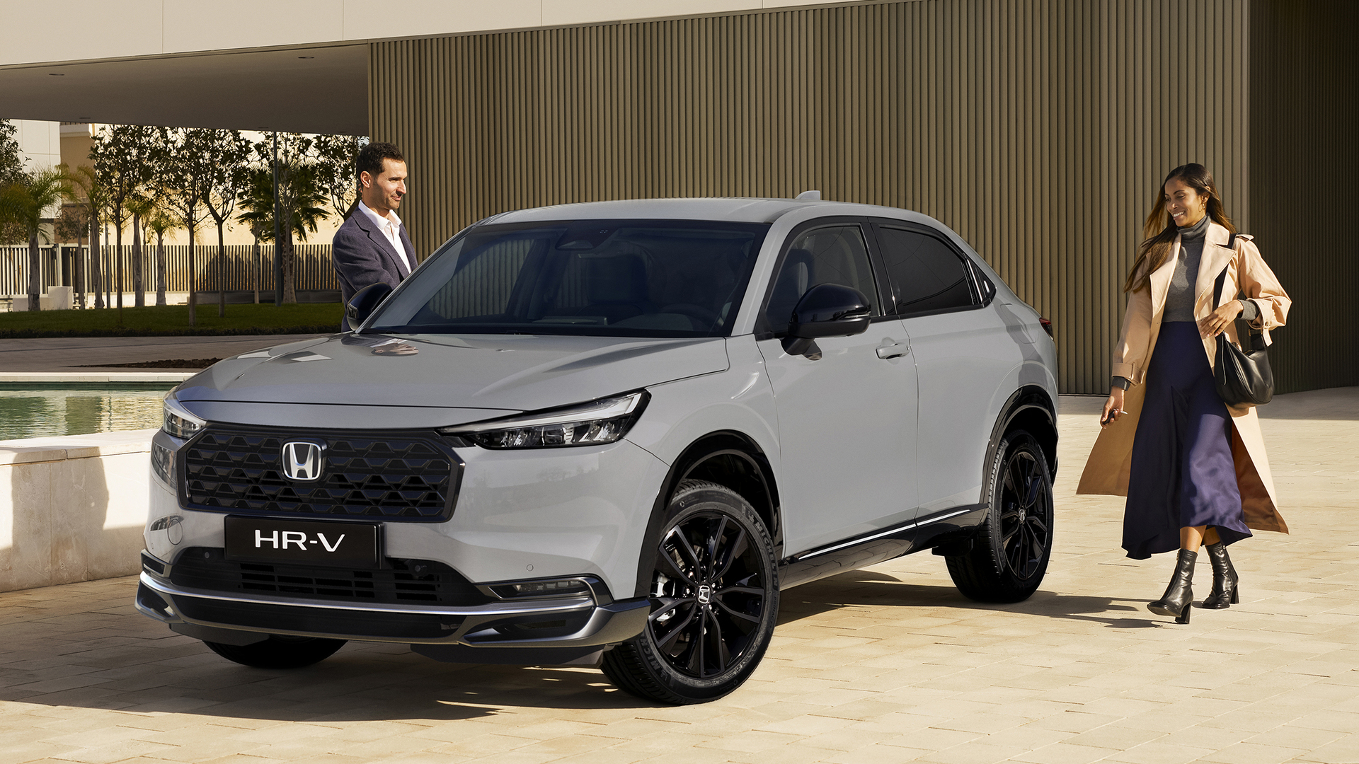 Biały Honda HR-V jedzie w kierunku kamery po dwupasmowej drodze, otoczonej wysoką, złotą trawą, pod błękitnym niebem.