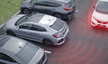 Honda Sensing — samochód na parkingu z ilustracją monitorowania zbliżających się pojazdów podczas cofania oraz informacji o martwym pola widzenia.