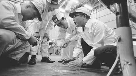 Soichiro Honda i pracownicy fabryki w białych kombinezonach.