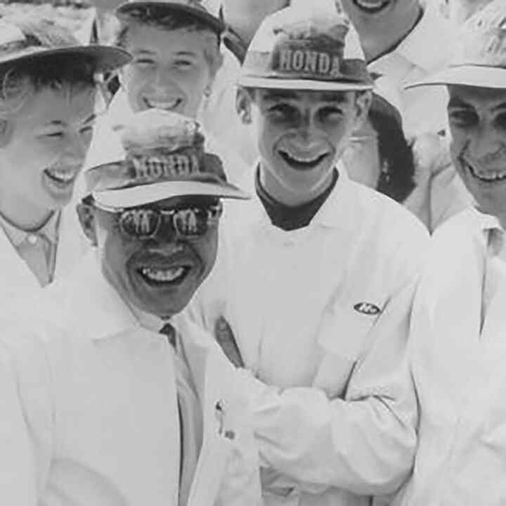 Soichiro Honda i pracownicy fabryki w białych kombinezonach.