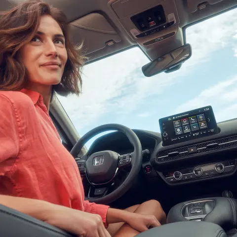 Kobieta siedząca w fotelu kierowcy i używająca ekranu systemu informacyjno-rozrywkowego w hybrydowej Hondzie ZR-V.