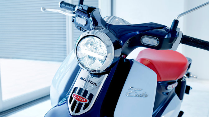 Honda Super Cub, zaparkowana w nowoczesnej scenerii.
