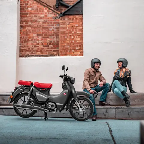 Honda Supercub 125 - ujęcie przedstawiające stojący motocykl z kierowcą i pasażerem