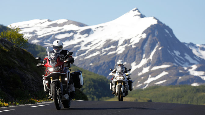 Dwa motocykle jadące drogą na tle ośnieżonych górskich szczytów w oddali.