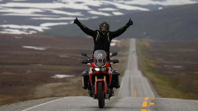 Mężczyzna na Hondzie Africa Twin z rękami uniesionymi do góry na drodze w Nordkapp.