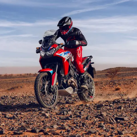 Model prowadzący motocykl CRF1100L Africa Twin w skalistym terenie na pustyni.