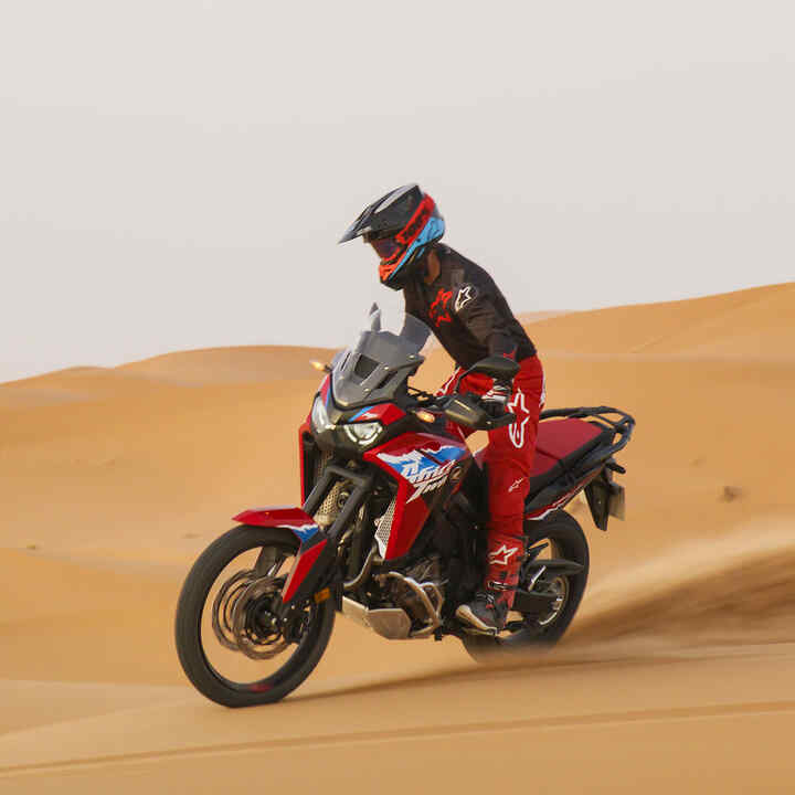 Model jadący motocyklem CRF1100L Africa Twin bike po drodze w pustynnym otoczeniu.