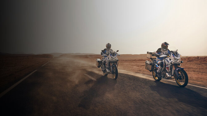 Zdjęcie motocyklistów od przodu (w ujęciu 3/4) na motocyklach CRF1100 Africa Twin Adventure Sports jadących po pustyni. 
