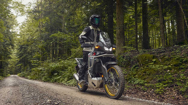 Model jadący na Hondzie XL750 Transalp w leśnej scenerii.