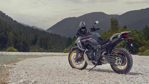Kierowca trzymający motocykl XL750 Transalp w górskiej scenerii.