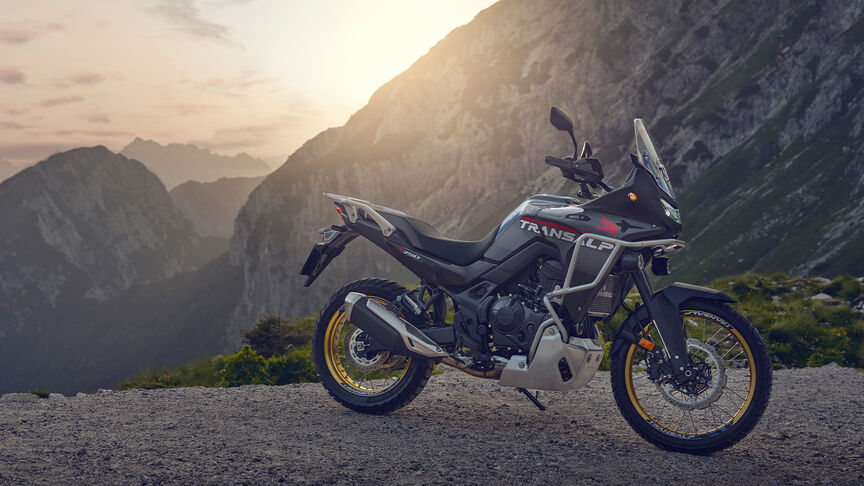 Model jadący motocyklem XL750 Transalp w leśnej scenerii.