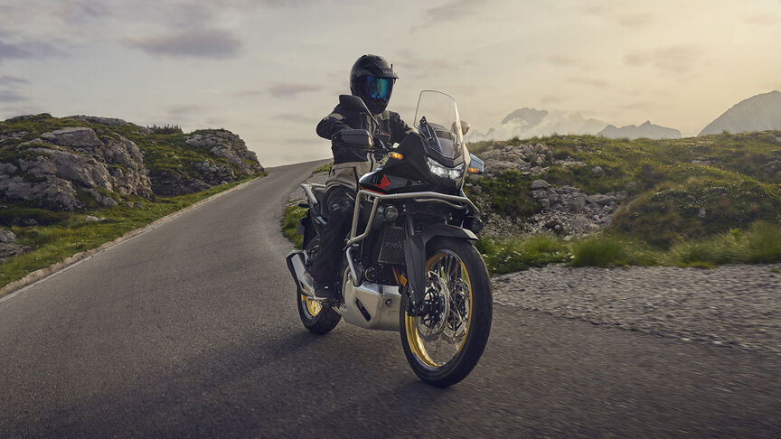 Model jadący motocyklem XL750 Transalp w leśnej scenerii.