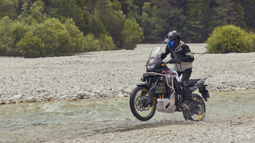 Model jadący motocyklem XL750 Transalp w leśnej scenerii.