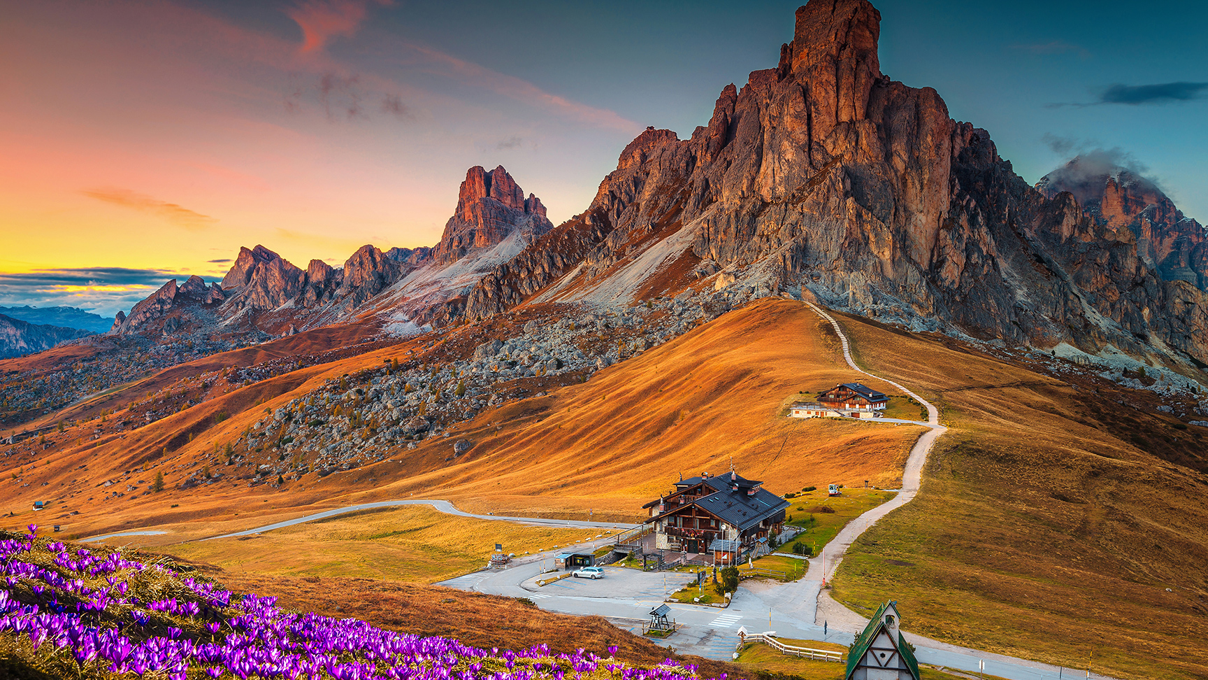 Wspaniała alpejska sceneria z wiosennymi krokusami na wzgórzach i spektakularnym widokiem gór o zachodzie słońca, przełęcz Giau, Dolomity, Włochy, Europa