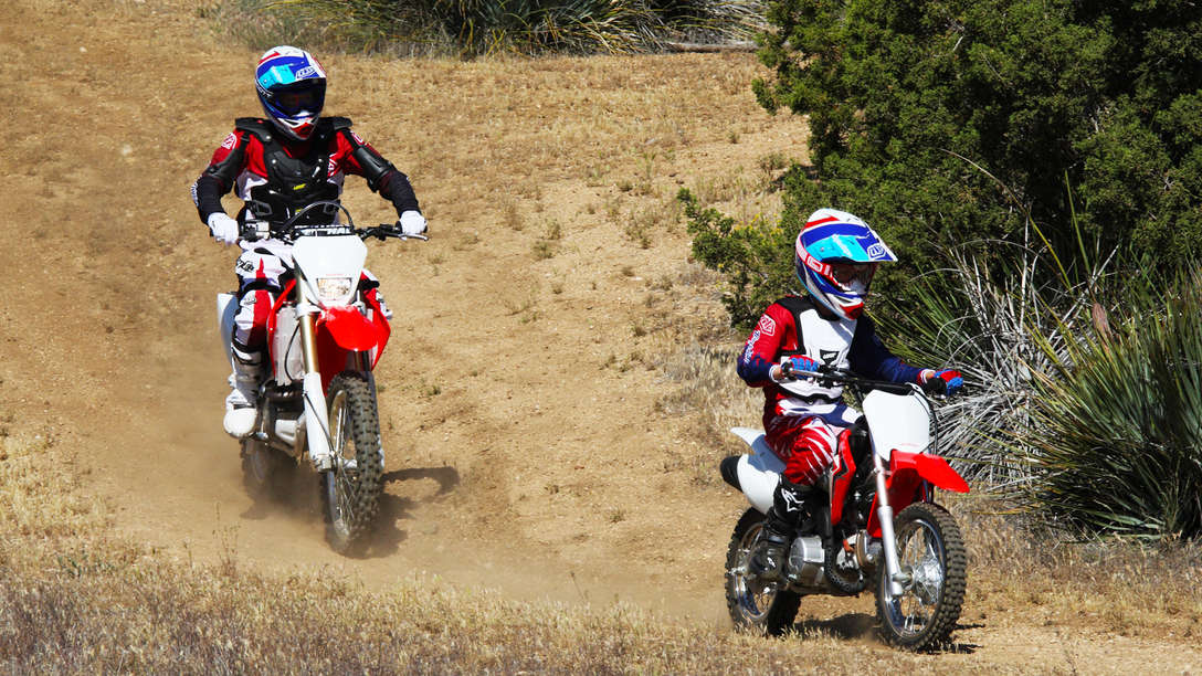 CRF150R — widok z boku 3/4 z prawego profilu przedstawiający motocykle z kierowcami na torze wyścigowym.