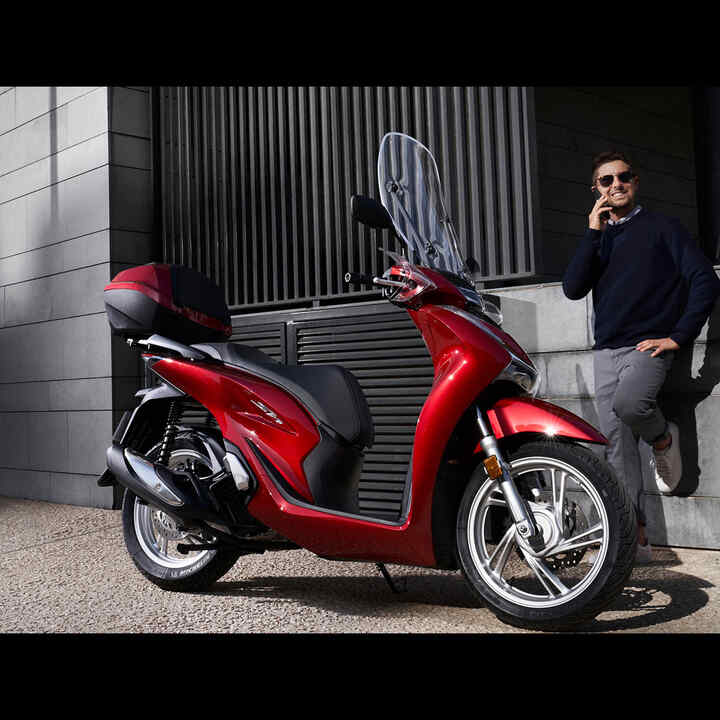 Mężczyzna rozmawiający przez telefon stoi obok skutera Hondy.