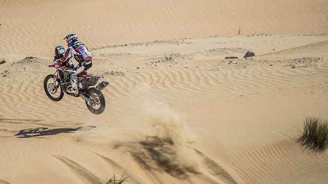 Honda CRF450 podczas jazdy przez piaszczyste wydmy — widok z tyłu.