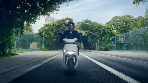 Widok z przodu na modela jadącego motocyklem Honda CUV e w mieście.