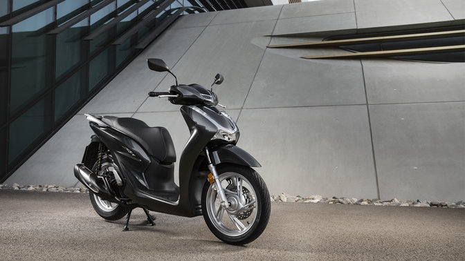 Honda Sh125i z górnym kufrem i szybą na ulicy.