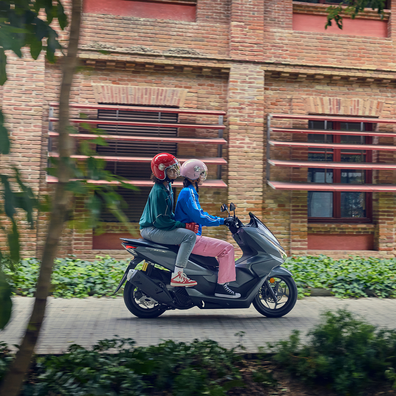 Boczne ujęcie modeli jadących na motocyklu PCX125 w mieście.