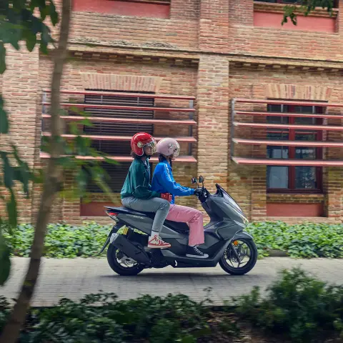 Boczne ujęcie modeli jadących na motocyklu PCX125 w mieście.