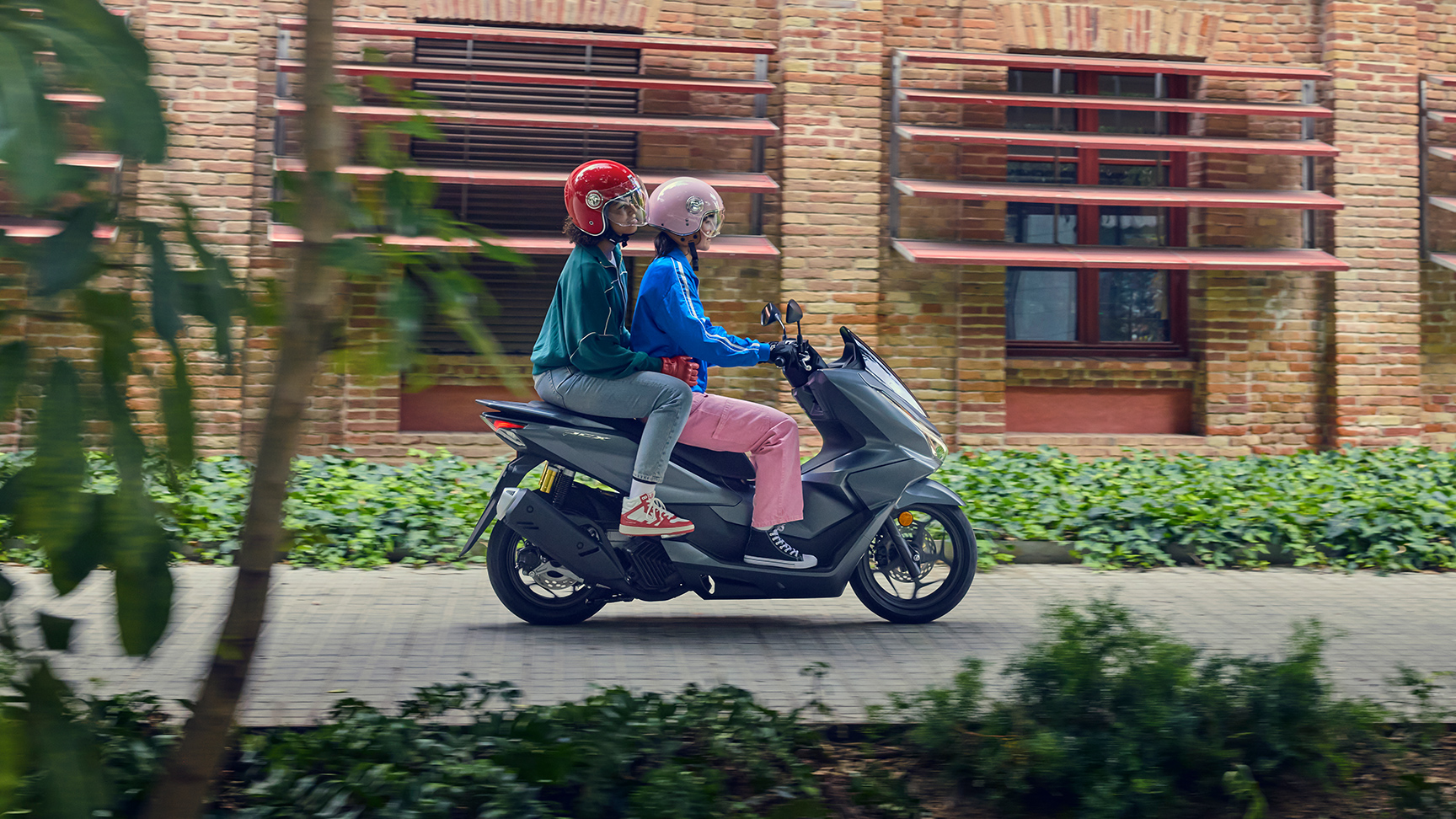 Boczne ujęcie modeli jadących na motocyklu PCX125 w mieście.