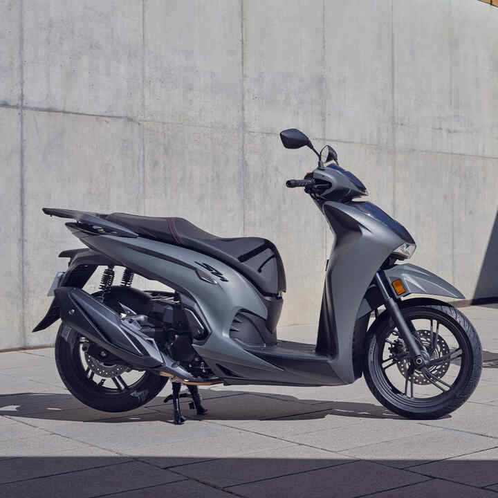 Dwie stojące Hondy SH350i na zewnątrz budynku. 