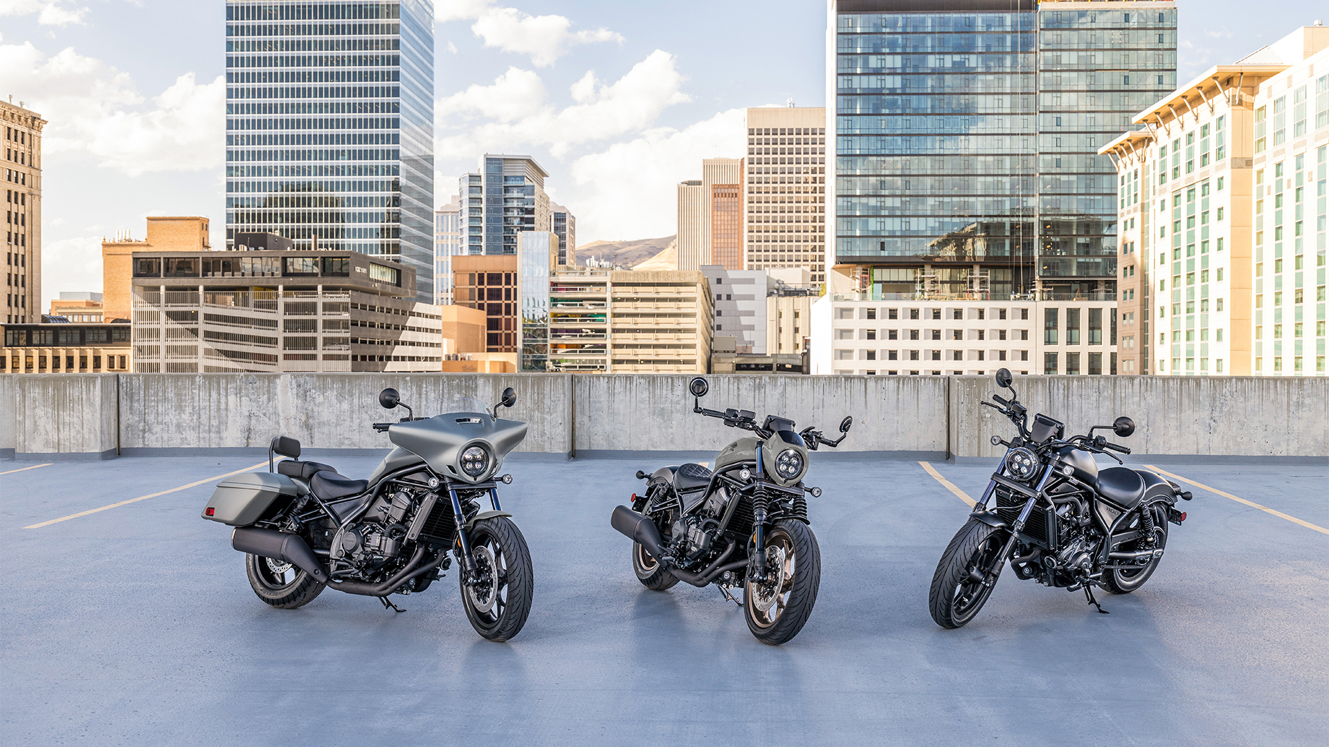 Trzy motocykle CMX1100 na zewnątrz, przed nowoczesnymi budynkami.