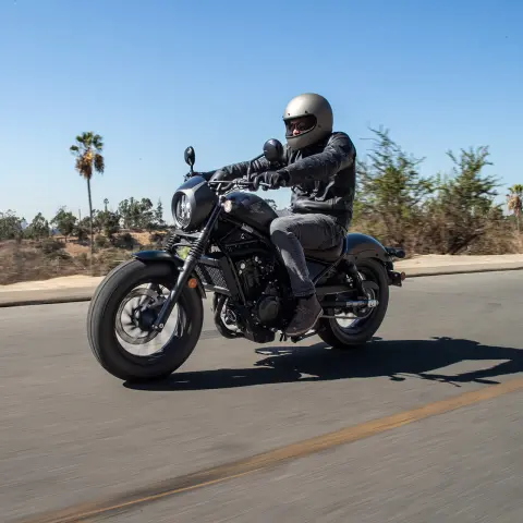 Honda CMX500 Rebel z motocyklistą jadącym drogą. 