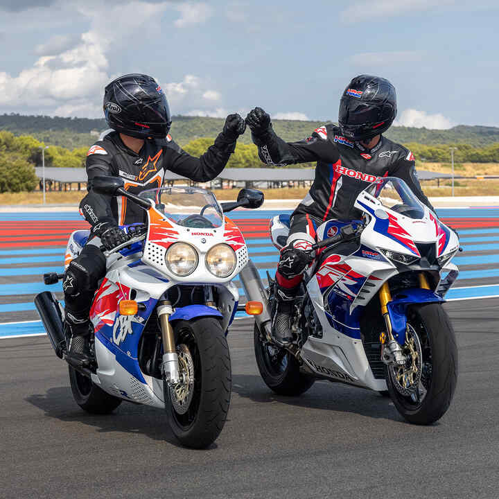 Dwóch kierowców przybijających pięści na torze wyścigowym siedząc na Hondach Fireblade sfotografowanych od przodu.