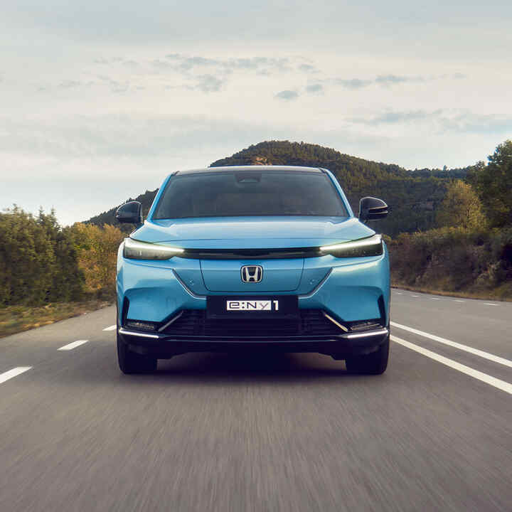 Honda e:Ny1 i Honda e przejeżdżające obok farmy wiatrowej. 